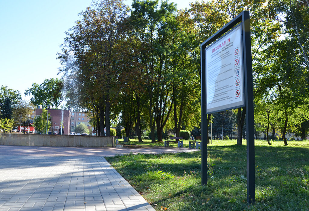 Tablica informacyjna zewnętrzna w parku jako element małej architektury miejskiej.